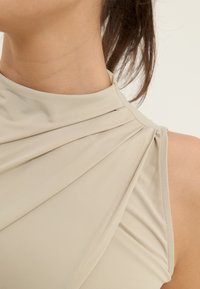 Gros plan sur le cou et l'épaule d'une personne portant un haut sans manches couleur beige avec des plis de tissu doux.