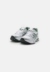 White athletic shoes with green accents, mesh upper, silver details, and a textured black sole. Features laces and a padded collar.