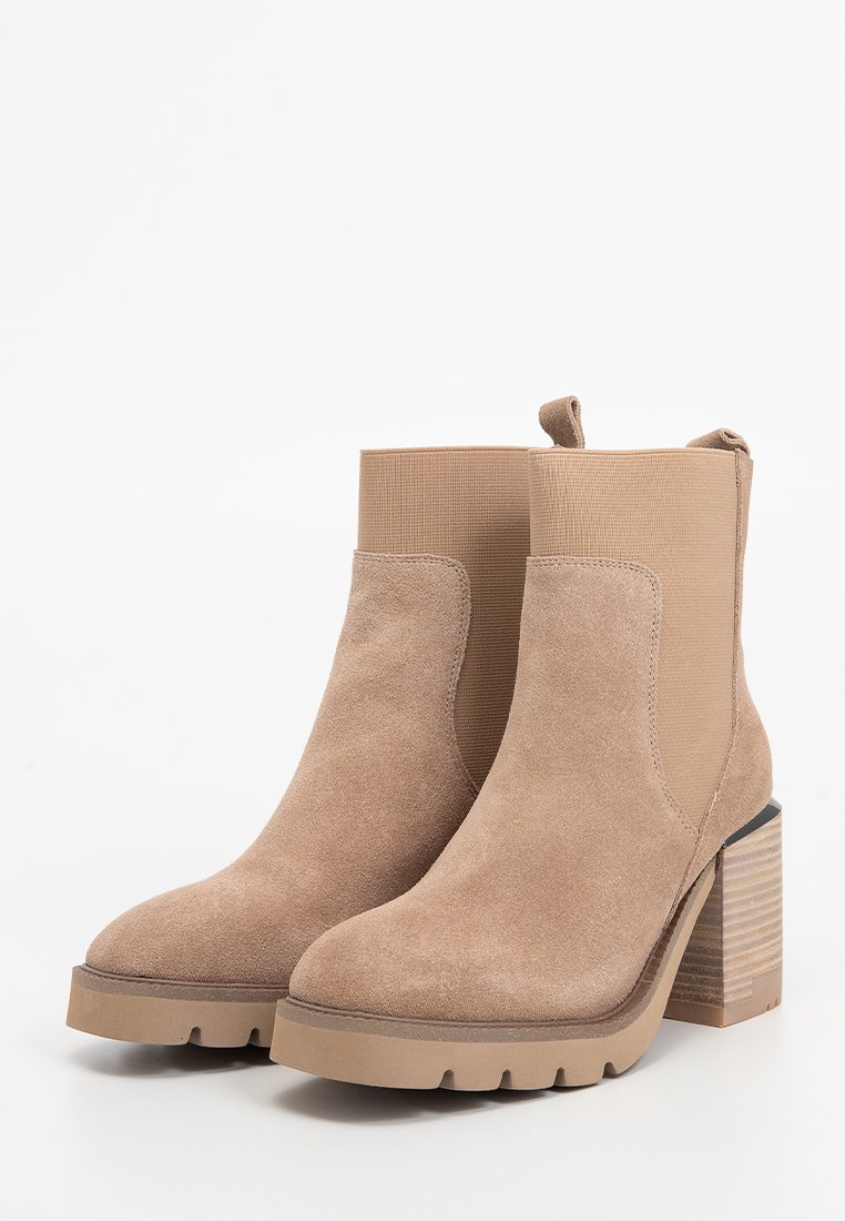 Botas de tobillo beige de ante con paneles elásticos a los lados, un tacón bloque texturizado y una suela de goma con un patrón de zigzag.