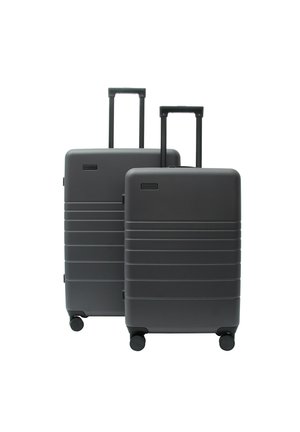 Zwei dunkelgraue Hartschalenkoffer mit ausgezogenen Griffen und vier Rädern, einer größer hinter einem kleineren, vor weißem Hintergrund.