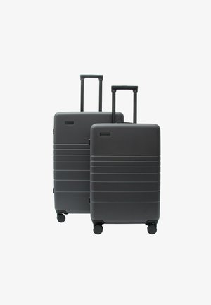 Zwei dunkelgraue Hartschalenkoffer mit ausgezogenen Griffen und vier Rädern, einer größer hinter einem kleineren, vor weißem Hintergrund.