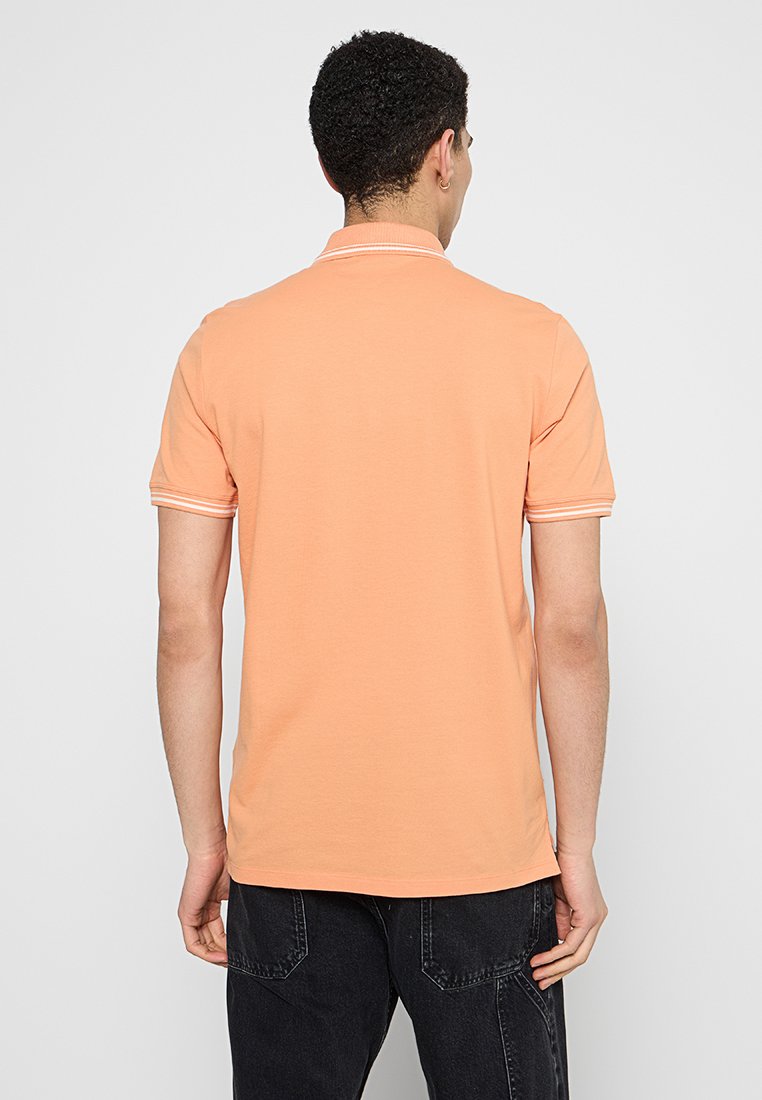 Koszulka polo w jasnym pomarańczowym kolorze, z krótkimi rękawami, miękką teksturą i białymi paskami na kołnierzyku i rękawach.