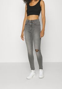 Vaqueros ajustados grises de talle alto con un detalle desgastado en la rodilla, combinados con un top corto negro y zapatillas blancas. Textura suave de mezclilla.