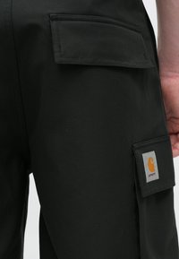 Μαύρο παντελόνι καμπαρντίνα με λεία υφή, διαθέτει δύο πίσω τσέπες και ένα τετράγωνο μπαλώμα με πορτοκαλί λογότυπο στην δεξιά πίσω τσέπη.