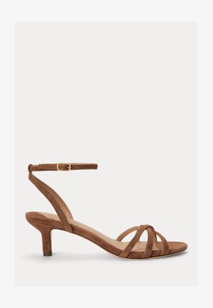 Sandale en daim marron avec des fines brides croisées, un petit talon kitten et une sangle de cheville avec une boucle dorée.