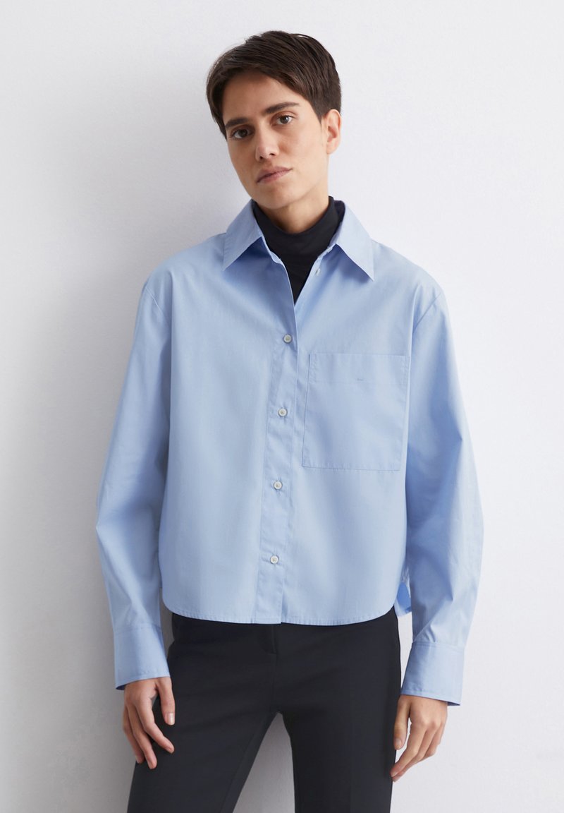 Lyseblå, cropped button-up skjorte med spidse krave, enkelt brystlomme og lange ærmer. Har letvægtsstof og en afslappet pasform.