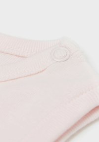 Jasnoróżowa tkanina o prążkowanej fakturze i zapięciem na zatrzask przy dekolcie. Gładkie wykończenie, prosty design.