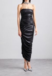 Černé bezramínkové šaty z lesklé látky, s nařasenými detaily po celém povrchu. Stylizované se stříbrným řetízkovým náhrdelníkem a metalickými špičatými podpatky.