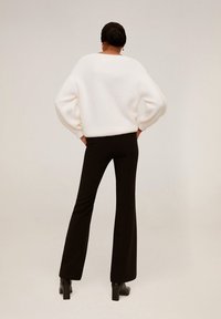 Pull blanc texturé avec des manches surdimensionnées associé à un pantalon noir évasé, sur un fond neutre.