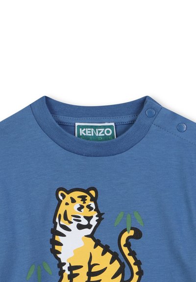 T-shirt en coton bleu avec un graphisme de tigre en orange et noir, agrémenté de détails en bambou vert. Comprend des boutons-pression sur l'épaule.