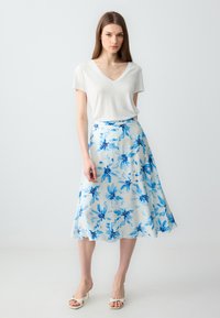 T-shirt bianco a V con una gonna fluida, lunga fino al ginocchio, caratterizzata da motivi floreali blu su uno sfondo chiaro. Sandali con tacco a blocco semplici.