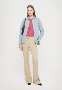 Camisa azul de botones sobre una blusa roja, combinada con pantalones acampanados beige y zapatos negros de punta. Diseño sencillo, tejido ligero y corte ajustado.
