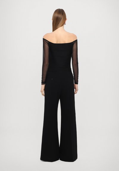 Melnas off-the-shoulder blūzes ar caurspīdīgām garām piedurknēm, pārī ar augstu jostasvietu melniem plaša griezuma biksēm ar aizmugurējām kabatām.