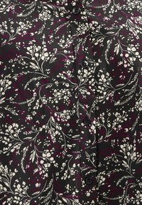Tessuto nero con motivo floreale in bianco e viola scuro, decorato con piccole foglie e bacche, presentato con bottoni neri disposti in una fila verticale.