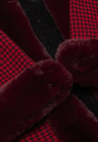 Rød og sort houndstooth-stof kombineret med dyb bordeaux faux fur-kant, der har en blød tekstur og kontrasterende mønstre.