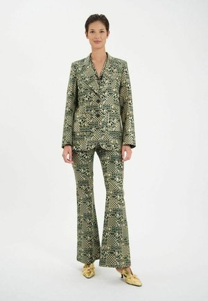 Costume à motifs verts et beiges avec pantalons évasés et veste à revers. Le matériau a une finition texturée. Les caractéristiques de design notables incluent des formes géométriques.