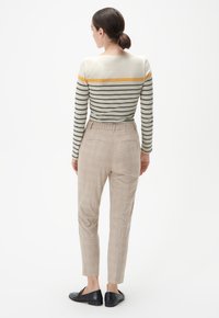 Pasekowany longsleeve w jasnym beżu, z szarymi i żółtymi paskami. Noszony z wysokim stanem, w kratkę, beżowymi spodniami i czarnymi butami.
