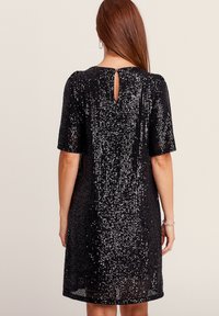 Schwarzes Kleid mit kurzen Ärmeln, einem Schlüsselrücken-Detail und einem strukturierten Design, das mit Pailletten verziert ist und für einen funkelnden Effekt sorgt.