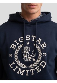 Tamsiai mėlynas džemperis su gobtuvu, išsiuvinėtu logotipu, vaizduojančiu liūtą, laurų vainiką ir tekstą "BIG STAR LIMITED". Surišimo virvutės su tamsiais galais. Minkšta medžiaga.