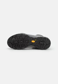 Chaussure de trail avec un dessus gris et une semelle en caoutchouc noir texturé. Présente un motif de crampons agressif et un logo Vibram sur la semelle.