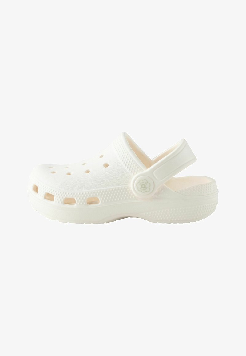 Sabot blanc aéré avec semelle texturée et bride de talon ajustable ornée d'un bouton en forme de fleur sur fond uni.