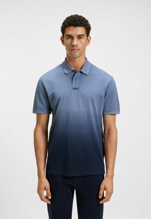Mann trägt ein kurzärmliges blaues Poloshirt mit Farbverlauf und Kragen sowie dem "BOSS"-Logo und steht vor einem schlichten hellen Hintergrund.