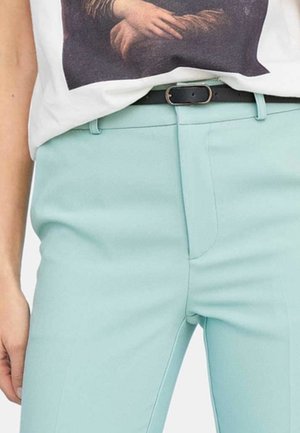 Person iført lyseblå bukser med sort bælte og en hvid skjorte med et trykt motiv af krydsede hænder.