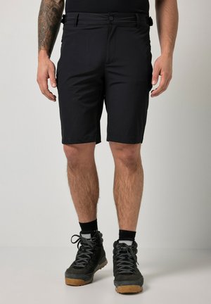 Mand iført sorte shorts, sorte sokker og sorte vandrestøvler, der står mod en ensartet lys baggrund.