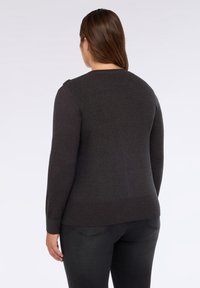 Maglione grigio scuro, texture a coste, colletto rotondo, maniche lunghe, con bottoni sulle spalle. Abbinato a jeans neri aderenti.