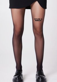 Collant neri trasparenti con la frase "FUTURE IS FEMALE" stampata sulla coscia superiore. Tessuto liscio, abbinati a mocassini neri lucidi.
