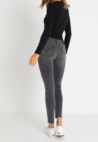 Top ajustado negro de manga larga combinado con jeans ajustados grises que cuentan con bolsillos traseros y dobladillo deshilachado, complementado con zapatillas blancas.