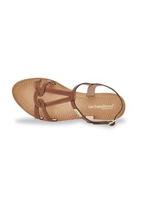 Sandale en cuir brun avec une semelle plate, dotée d'un design à sangle en T, de détails de couture et d'une fermeture à boucle sur la sangle de cheville.
