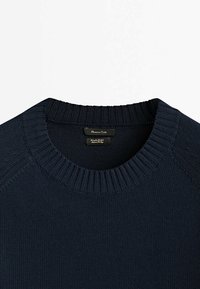 Pull en tricot bleu marine à col ras du cou avec un col côtelé et une étiquette de marque visible à l'intérieur de l'encolure.