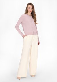 Cardigan lung cu mâneci lungi, roz deschis, cu decolteu rotund și nasturi din perlă, asortat cu pantaloni largi crem. Texturi netede, croială lejeră.