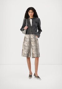 Chaqueta de mezclilla negra con un diseño corto, pantalones cortos de estampado de serpiente gris y zapatos de tacón metálicos, que muestran texturas y patrones distintos.