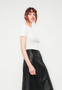 Fitted white ribbed top with short sleeves paired with a long black leather skirt featuring vertical seams and a smooth texture.