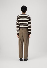 Striped brown and white sweater with a crew neck, paired with brown textured pants. Black footwear is visible. Back view against a plain background.