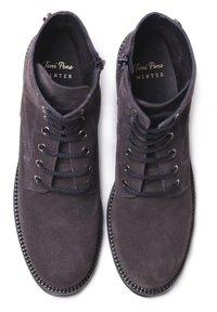 Botas de ante gris oscuro hasta el tobillo con diseño de lazada de cinco ojales, suela de goma y costura texturizada a lo largo del borde de la suela.