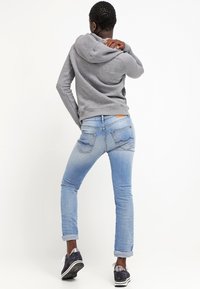 Grå bomullshuvtröja med dragsnöre, bärs med ljusblå denimjeans. Sneakers har en mörk överdel med silverdetaljer och en vit sula.