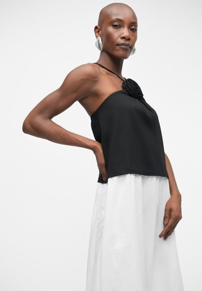 Haut sans manches noir avec une rosace au niveau du col, associé à une jupe blanche fluide, arrivant aux genoux. Tissu lisse, design minimaliste.