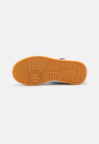 White sneaker sole with a textured, gum-colored rubber bottom. Features circular and linear tread patterns and a circular logo detail.