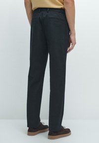 Pantalons gris foncé avec une coupe droite, fabriqués dans un tissu lisse. Deux poches arrière et une taille plate visibles.