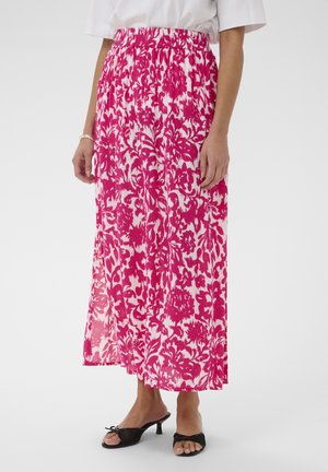 Femme portant une jupe midi fleurie rose et blanche à taille élastique, un haut blanc à manches courtes, un bracelet argenté, et des sandales à talons noires.