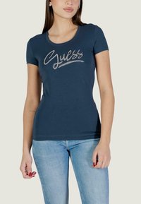 T-shirt aderente blu navy in cotone, con logo "Guess" glitterato sul petto. Maniche corte e scollo rotondo.