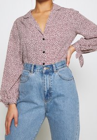 Långärmad skjorta med krage i vitt med ett mönster av röda och svarta prickar, matchad med högmidjade, ljusblå denimjeans med fickor.