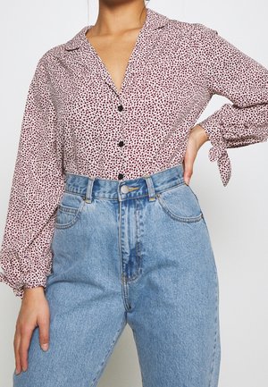 Camicia a maniche lunghe con colletto, di base bianca e motivo a macchie rosso-nero, abbinata a jeans in denim leggeri a vita alta di colore blu, con tasche.