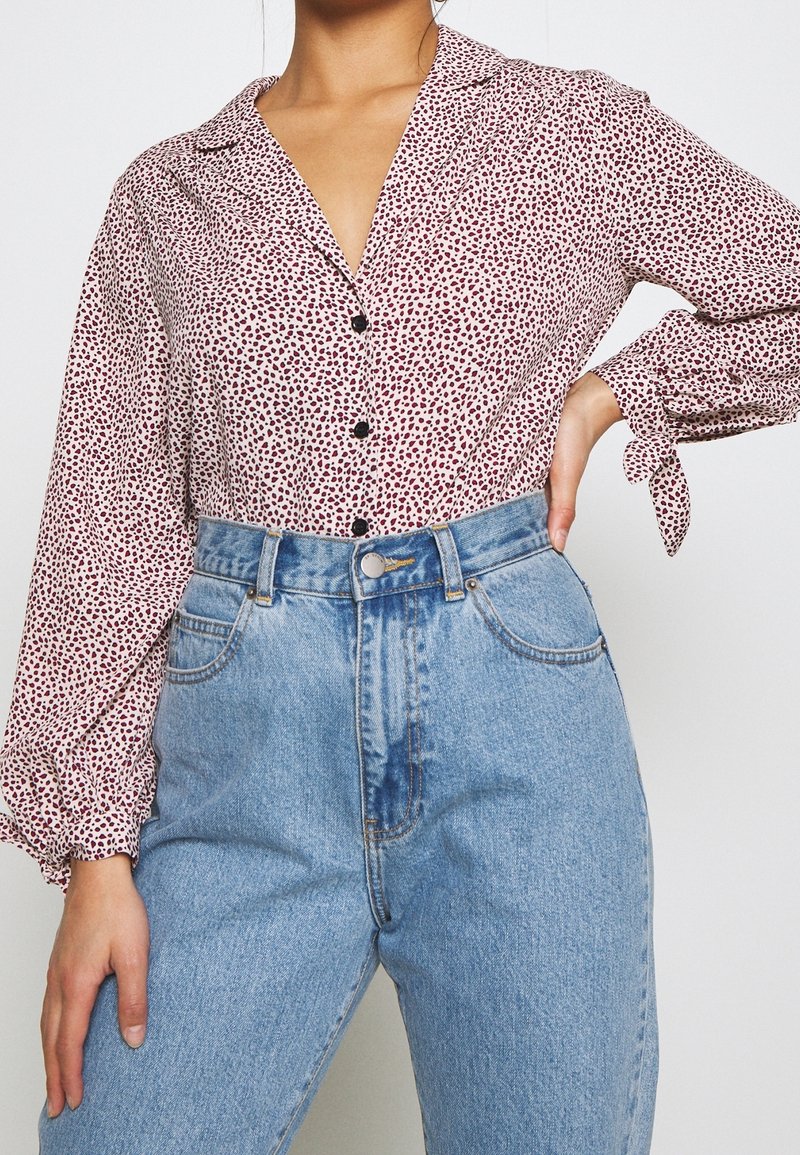 Långärmad skjorta med krage i vitt med ett mönster av röda och svarta prickar, matchad med högmidjade, ljusblå denimjeans med fickor.