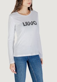Modello che indossa una camicia bianca a maniche lunghe con "LIU·JO" stampato sul davanti, abbinata a jeans blu. Look semplice e stiloso per il tempo libero.