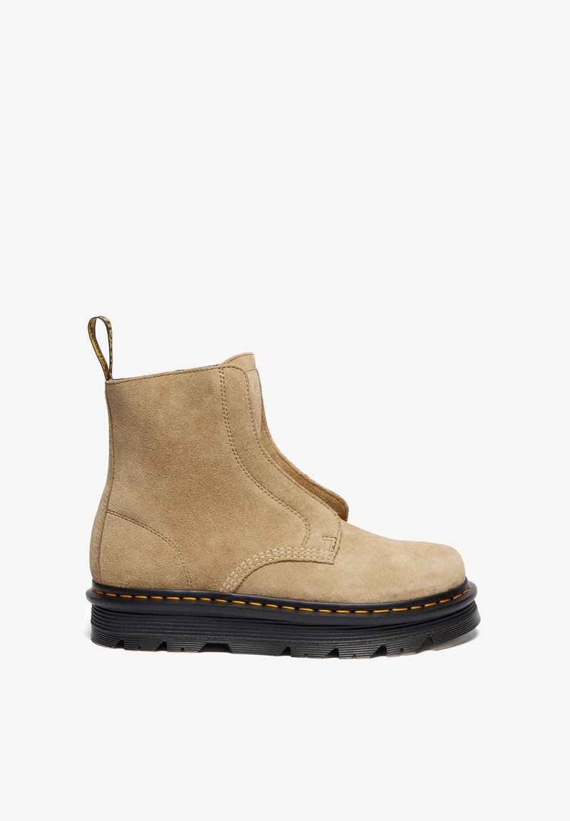 Bottine beige en daim avec semelle noire épaisse, couture jaune, languette de tirage au talon, et dessus lisse sans lacets ni fermetures visibles.