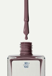 Nagellacksborste med dammig mauve-lack som droppar ovanför en öppen kvadratisk glasflaska märkt "80+ / 100" mot en vit bakgrund.